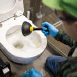technician using a plunger to clear a blocked toilet during plumbing unblocking work in napier and hastings